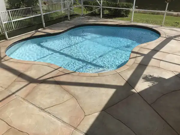 Tan stamped concrete pool deck resurfaced in a flagstone pattern, screened enclosure overlooking a canal
