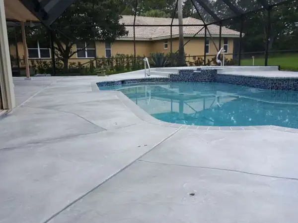 Smooth spray-textured grey concrete pool deck with blue accent tile, screened enclosure