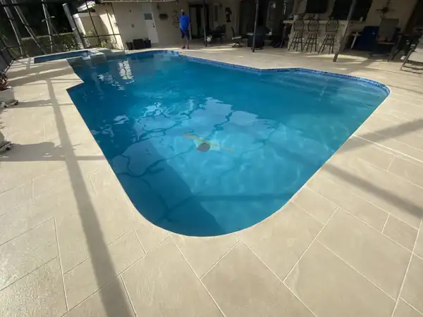 Tan stamped concrete pool deck in a screened enclosure with a swimmer in the pool