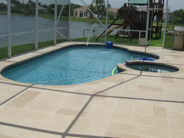 Tan textured concrete pool deck with an attached spa in a screened enclosure overlooking a lake