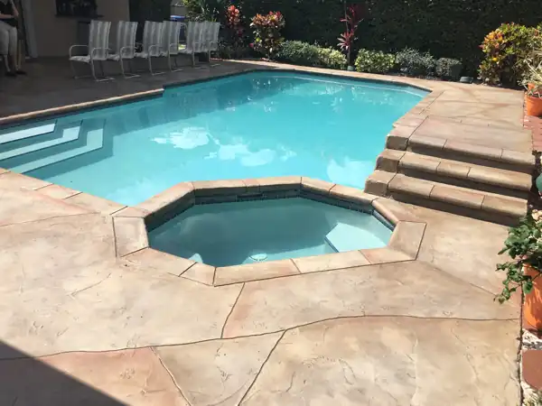 Tan and rust two-tone stamped concrete pool deck with steps down to an octagonal raised spa