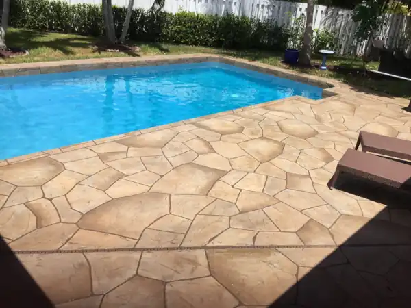 Tan stamped concrete flagstone pool deck beside a rectangular pool, white picket fence yard