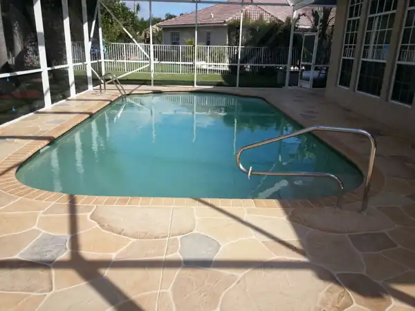 Tan two-tone stamped concrete flagstone deck beside a rectangular pool with brick coping, screened enclosure