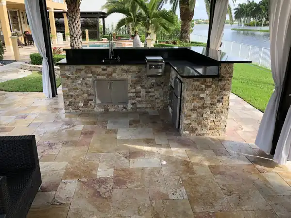 Custom outdoor kitchen with a stacked-stone base and black granite countertop, poolside with a lake view