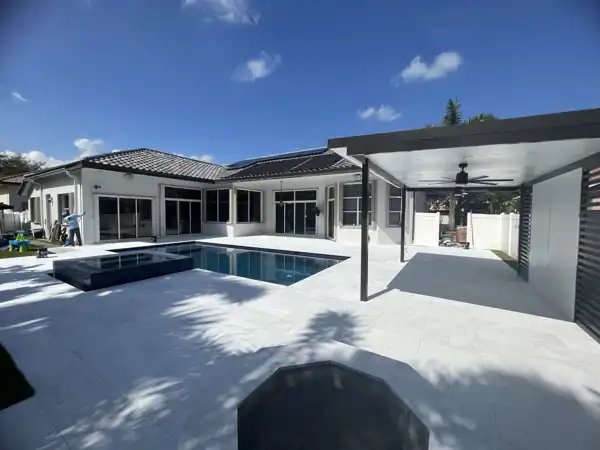 Aluminum patio cover with a ceiling fan over a pool and paver deck