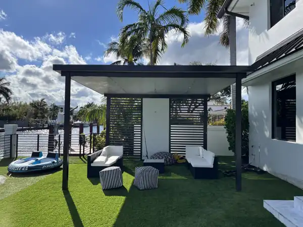 Aluminum pergola with a solid roof panel and privacy slat wall over a turf lawn on a waterfront lot