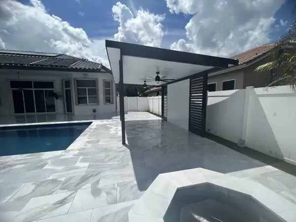 White aluminum patio cover with dark trim and ceiling fans extending along the house over a paver patio and pool