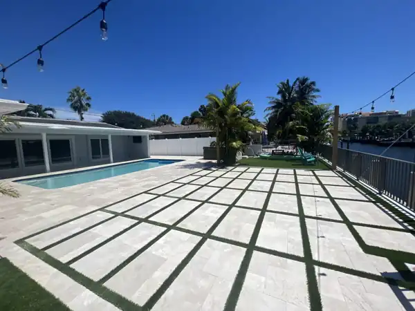 Artificial turf inlaid in a grid pattern between paver joints on a large patio beside the pool