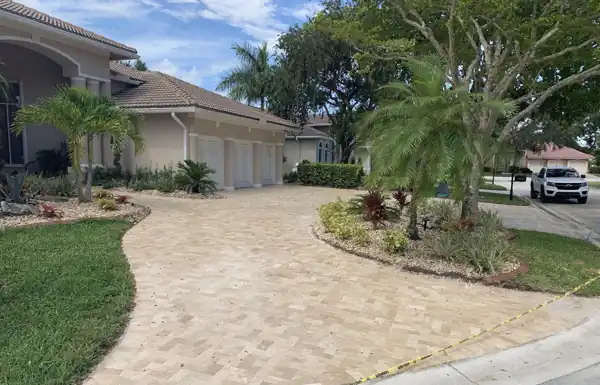 Curved tan paver driveway leading to a Mediterranean-style home with a tile roof and landscaped beds