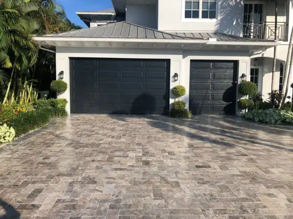 Two-car interlocking paver driveway leading to dark garage doors on a two-story South Florida home