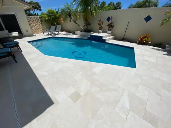 Rectangular pool with a raised tiled spa and travertine paver deck, patio furniture and blue accent tile on the privacy wall